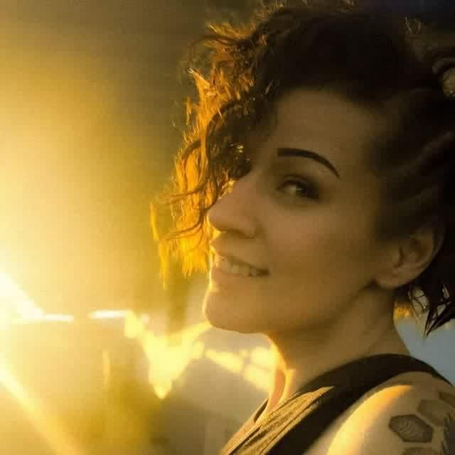 Portrait of artist Renee Grenade smiling in warm golden light, dark curly hair, tattoo on her shoulder.